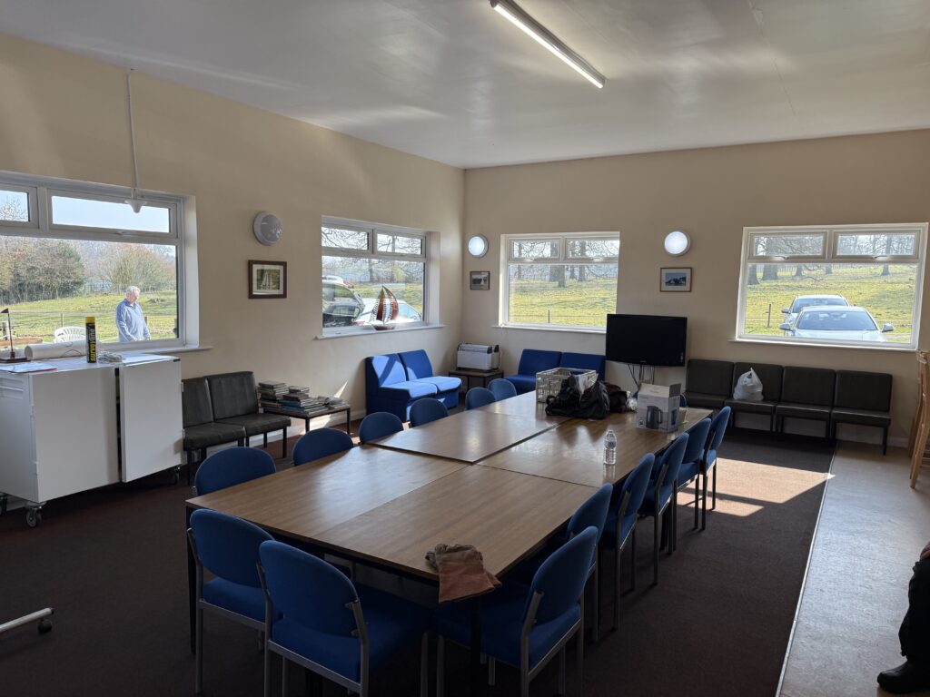 two cream interior smooth plastered walls with four windows, in the middle there is a set of tables with blue chairs around it.